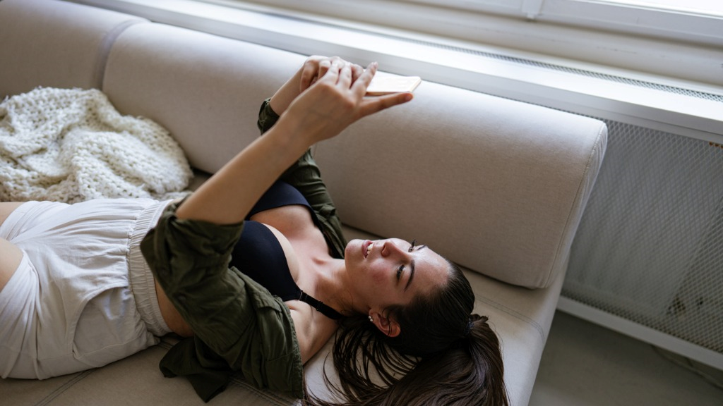 beautiful sexy brunette girl chatting on her mobile while laying on the couch